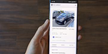 A hand holding a mobile device showing the Recurrent user experience